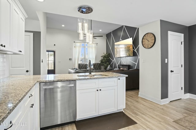 kitchen featuring light wood finished floors, white cabinets, open floor plan, stainless steel dishwasher, and a sink