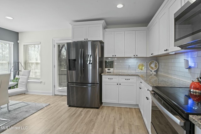 kitchen featuring appliances with stainless steel finishes, white cabinets, light wood-style flooring, and decorative backsplash