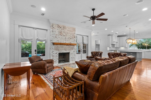 living room featuring ceiling fan with notable chandelier, light hardwood / wood-style floors, ornamental molding, and a fireplace