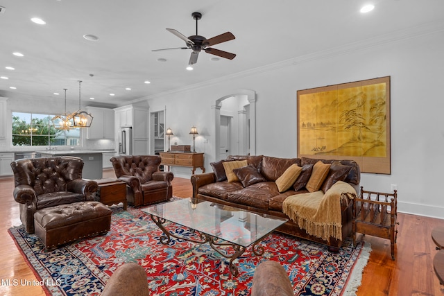 living room with ornamental molding, ceiling fan with notable chandelier, and hardwood / wood-style floors