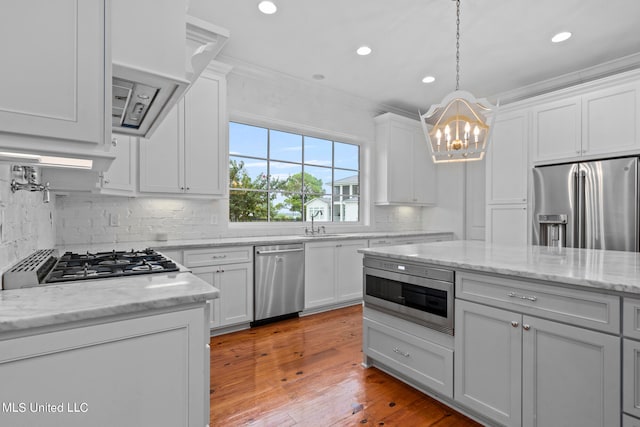 kitchen with light stone countertops, appliances with stainless steel finishes, light wood-type flooring, white cabinets, and crown molding