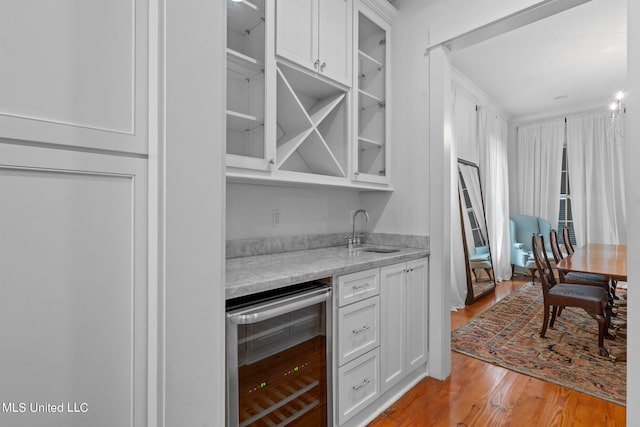 bar with sink, light stone countertops, beverage cooler, white cabinets, and light hardwood / wood-style floors