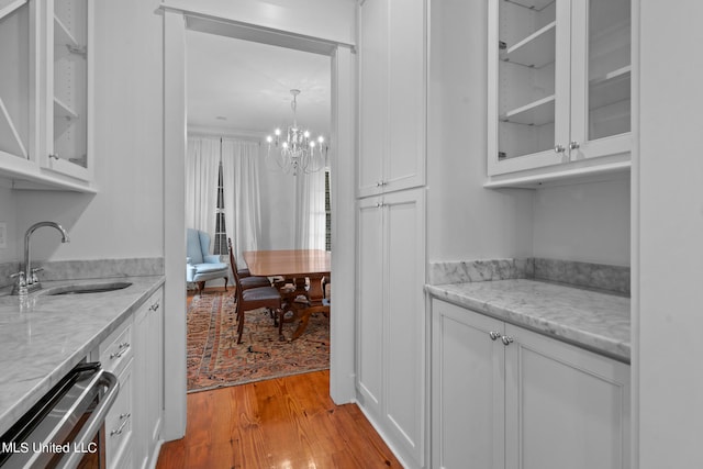 bar featuring white cabinets, light stone countertops, stainless steel dishwasher, light wood-type flooring, and sink