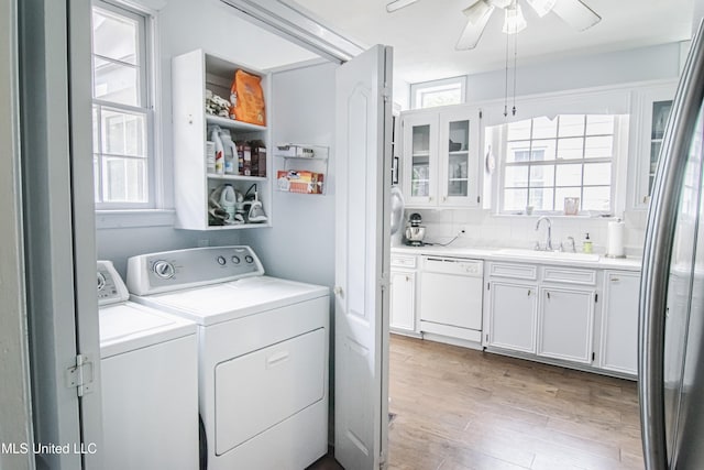 clothes washing area with laundry area, ceiling fan, a sink, light wood finished floors, and washing machine and dryer