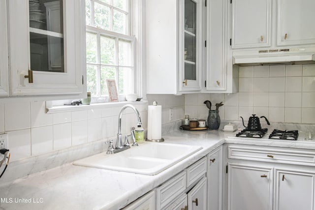 kitchen featuring tasteful backsplash, a sink, white cabinets, glass insert cabinets, and under cabinet range hood