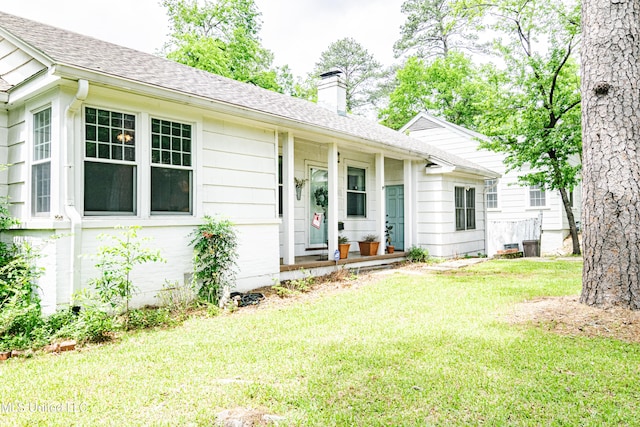 single story home with a shingled roof, a chimney, a porch, and a front yard