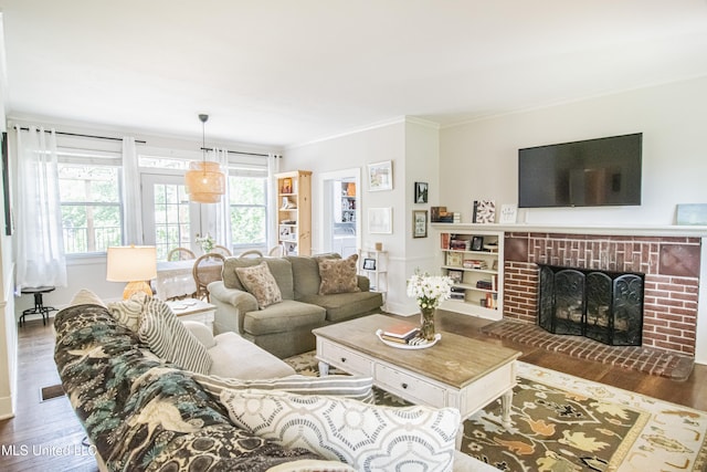 living area with ornamental molding, a brick fireplace, and wood finished floors