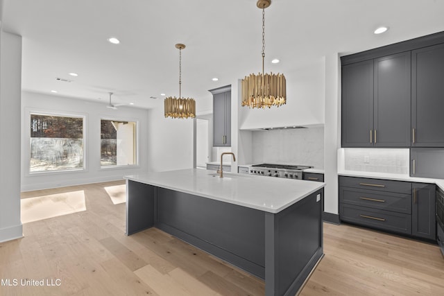 kitchen with decorative light fixtures, a sink, light countertops, light wood-type flooring, and a center island with sink