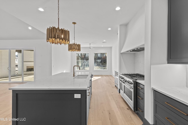 kitchen featuring light stone counters, a kitchen island with sink, double oven range, pendant lighting, and a sink