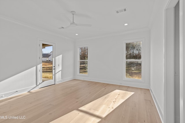 empty room with light wood-style floors, plenty of natural light, visible vents, and crown molding