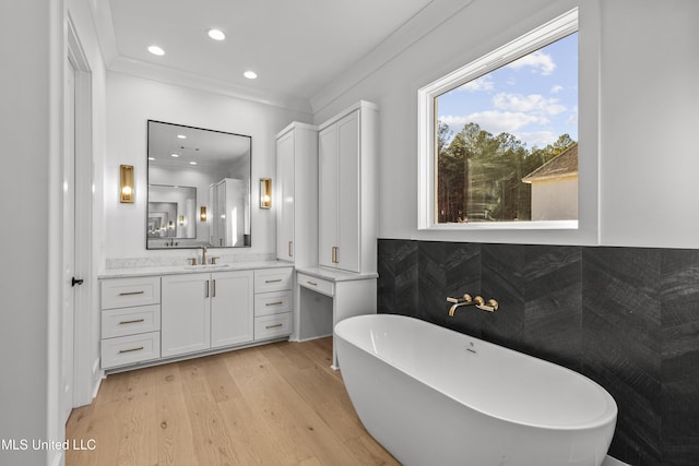 full bathroom featuring recessed lighting, wood finished floors, vanity, ornamental molding, and a soaking tub