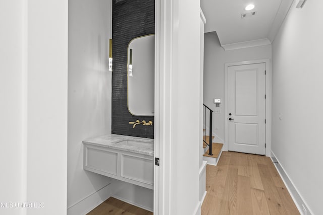 hallway featuring baseboards, visible vents, crown molding, light wood-type flooring, and a sink