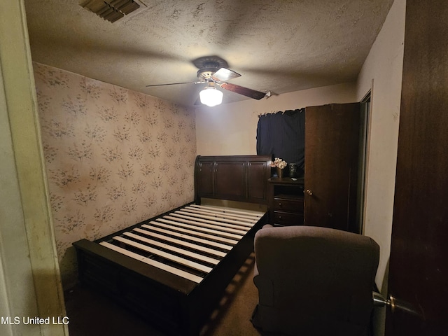 bedroom with a textured ceiling, ceiling fan, visible vents, and wallpapered walls