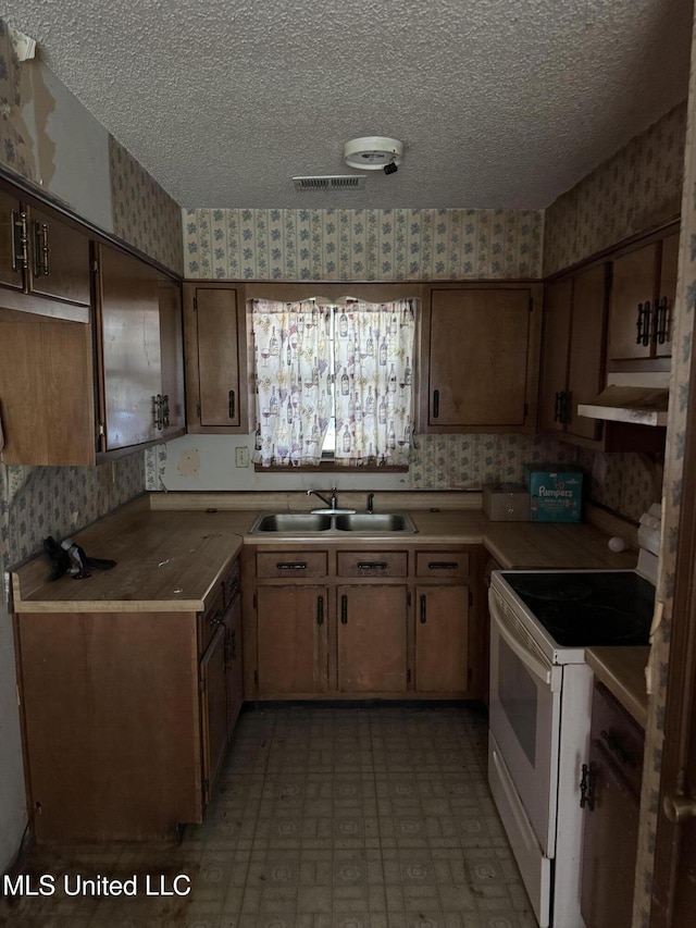 kitchen with white range with electric stovetop, wallpapered walls, a sink, under cabinet range hood, and a textured ceiling