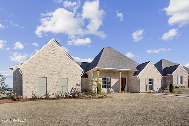 french provincial home featuring roof with shingles, a front yard, and brick siding