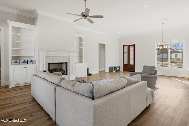 living area with baseboards, built in features, dark wood finished floors, crown molding, and a fireplace