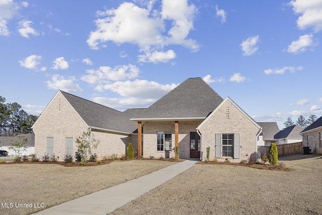 view of front of home featuring brick siding, roof with shingles, a front yard, central AC, and fence