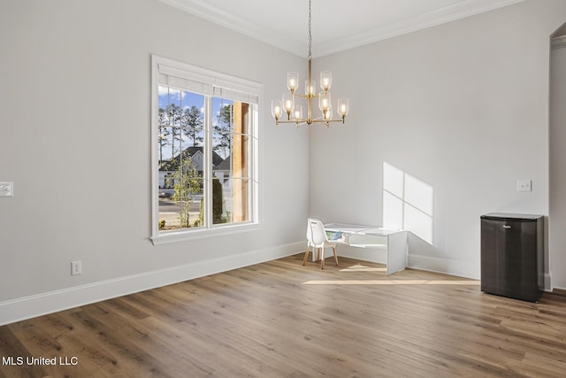 unfurnished dining area featuring ornamental molding, an inviting chandelier, baseboards, and wood finished floors