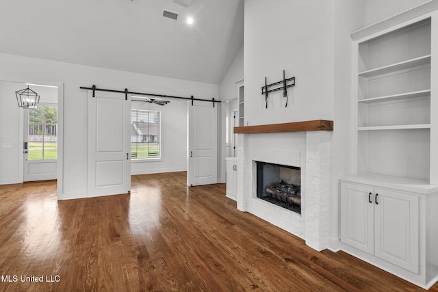 unfurnished living room featuring built in features, dark wood-style floors, a barn door, visible vents, and a brick fireplace