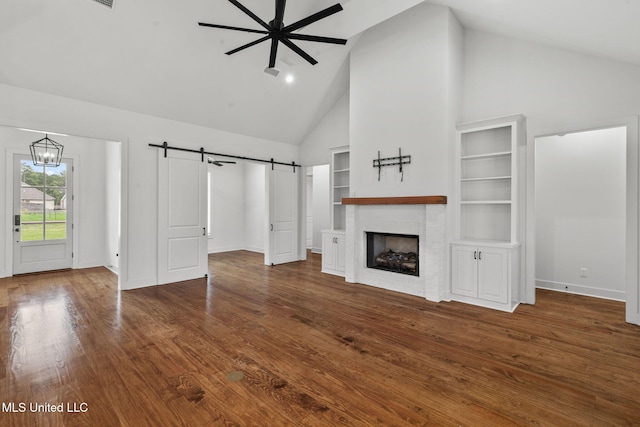 unfurnished living room with baseboards, a fireplace, a barn door, high vaulted ceiling, and wood finished floors