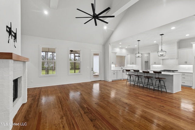 unfurnished living room with baseboards, a brick fireplace, ceiling fan, wood finished floors, and high vaulted ceiling