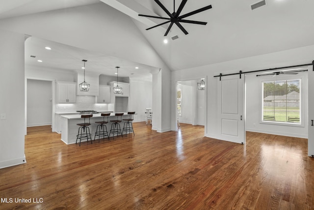 living room featuring wood finished floors, high vaulted ceiling, visible vents, and a barn door