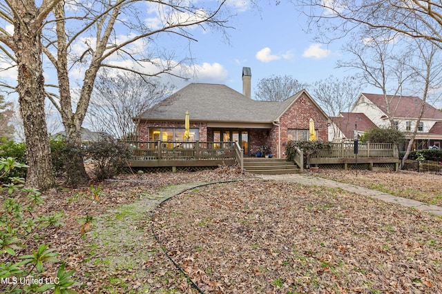 back of property with brick siding, roof with shingles, a deck, and a chimney