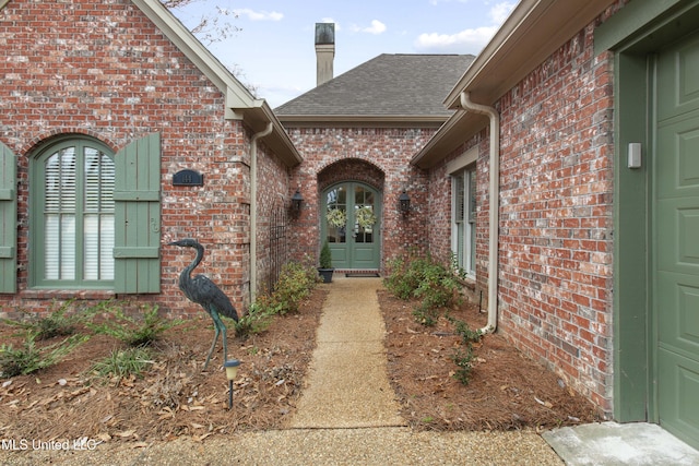 entrance to property featuring french doors, brick siding, and a shingled roof