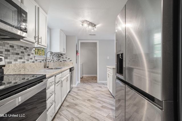2869 Honduras Dr, Gautier, MS 39553 - kitchen featuring appliances with stainless steel finishes, backsplash, white cabinetry, light wood finished floors, and light stone countertops