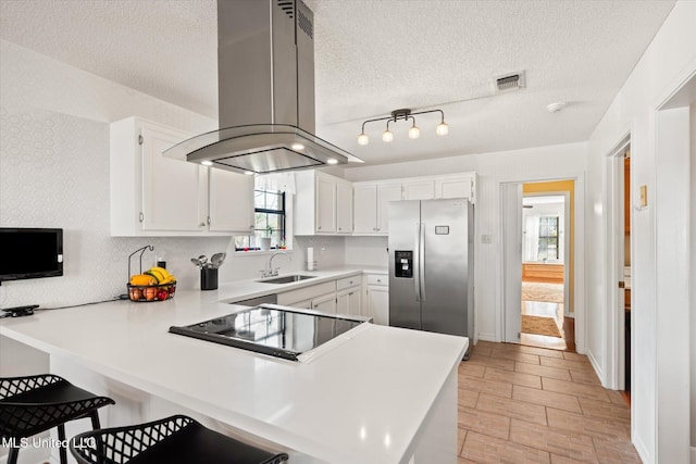 kitchen with visible vents, a peninsula, stainless steel refrigerator with ice dispenser, island range hood, and a sink