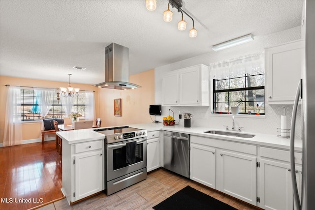 kitchen featuring appliances with stainless steel finishes, a peninsula, exhaust hood, white cabinetry, and a sink