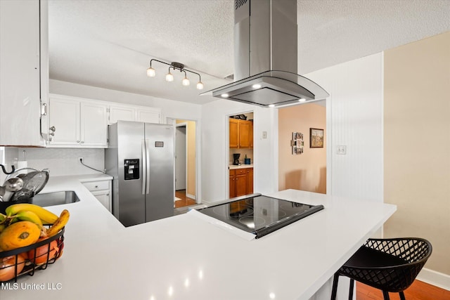 kitchen with stainless steel refrigerator with ice dispenser, a textured ceiling, island range hood, light countertops, and cooktop