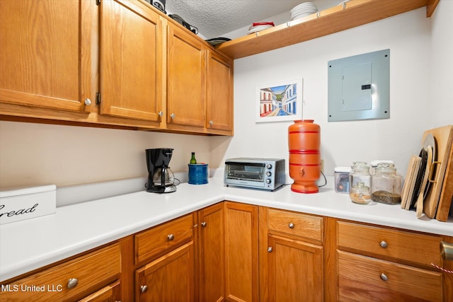 kitchen featuring brown cabinets, electric panel, a textured ceiling, a toaster, and light countertops