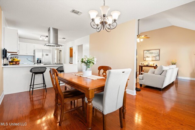 dining room with baseboards, visible vents, hardwood / wood-style flooring, vaulted ceiling, and ceiling fan with notable chandelier