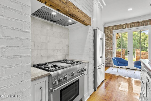 101 Lake Village Dr, Madison, MS 39110 - kitchen featuring light wood-style floors, wall chimney exhaust hood, white cabinetry, appliances with stainless steel finishes, and french doors