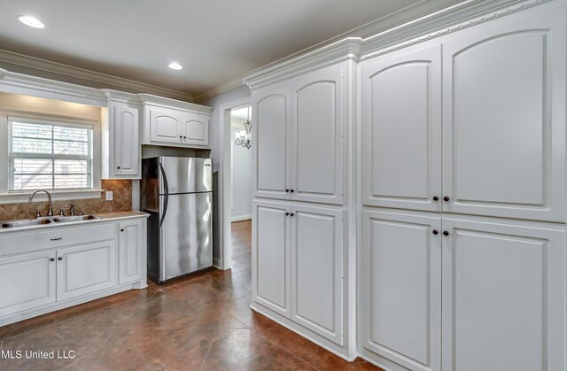 kitchen with crown molding, a sink, freestanding refrigerator, white cabinets, and decorative backsplash