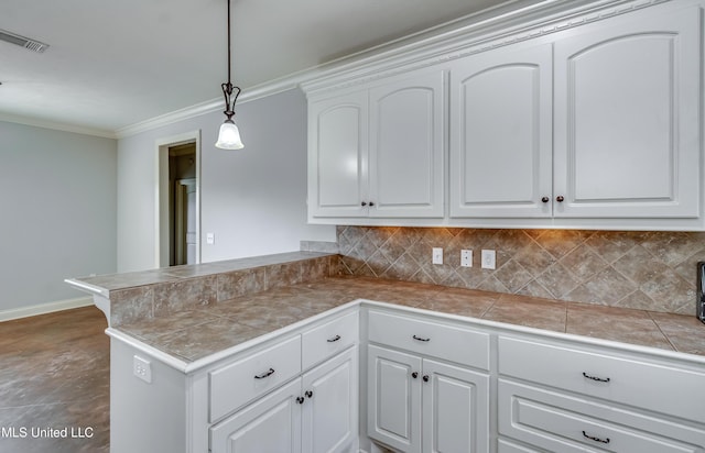 kitchen featuring visible vents, a peninsula, ornamental molding, tasteful backsplash, and tile countertops