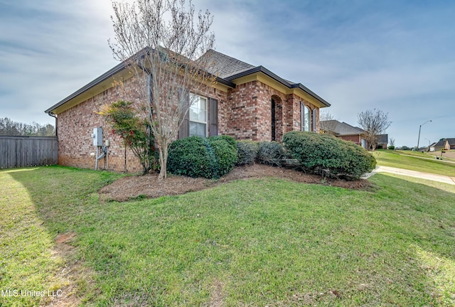 view of property exterior featuring brick siding, fence, and a yard