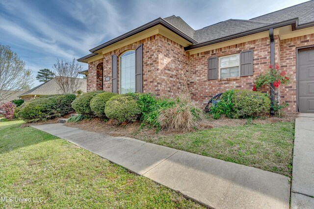 view of side of property with roof with shingles, brick siding, a yard, and an attached garage