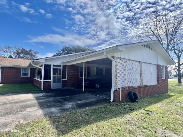 view of side of property with aphalt driveway, brick siding, a sunroom, a yard, and a carport