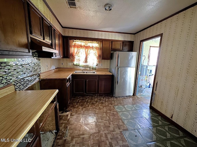 208 Cedar Dr, Diberville, MS 39540 - kitchen with freestanding refrigerator, under cabinet range hood, wallpapered walls, crown molding, and a textured ceiling