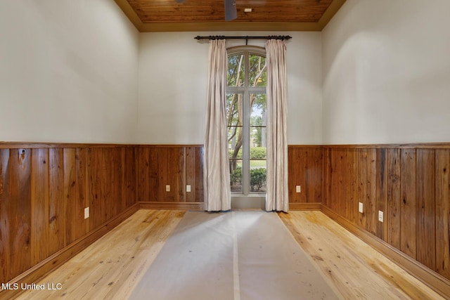empty room featuring wood ceiling, wooden walls, wainscoting, and hardwood / wood-style flooring