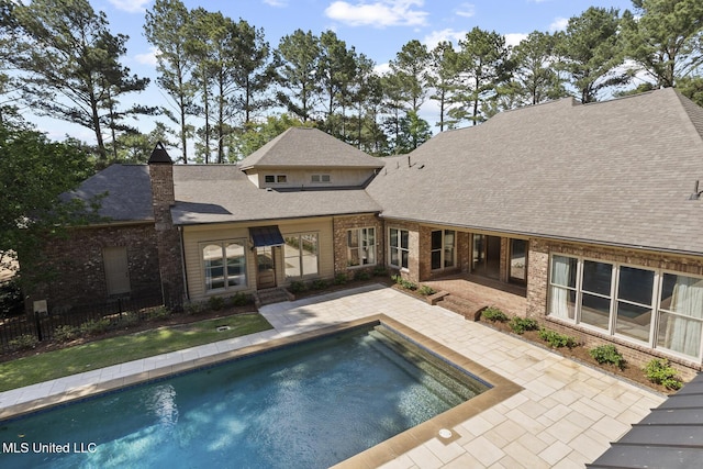 rear view of house featuring fence, a shingled roof, brick siding, an outdoor pool, and a patio area