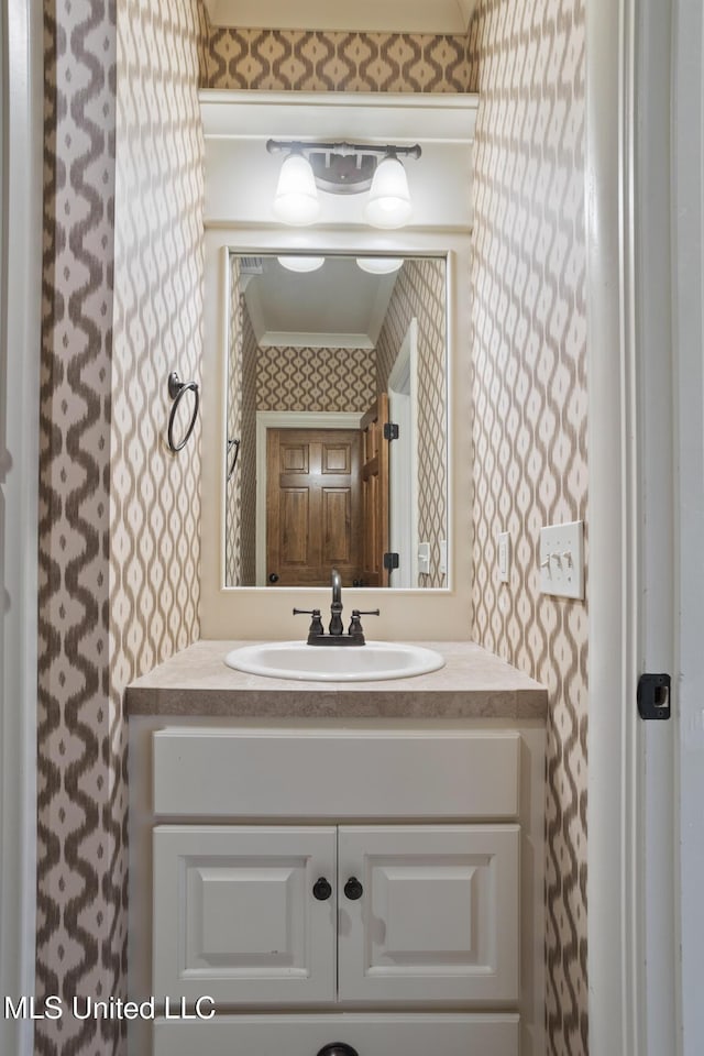 bathroom with vanity, ornamental molding, and wallpapered walls