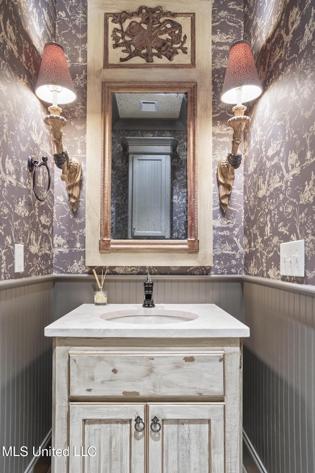 bathroom featuring vanity, wallpapered walls, and a wainscoted wall