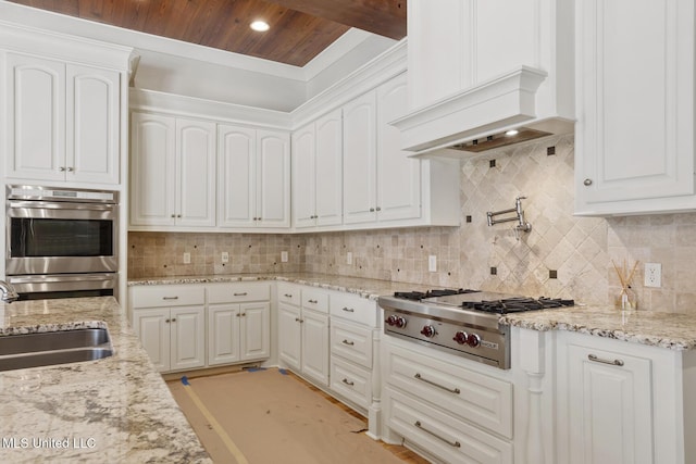 kitchen with tasteful backsplash, a sink, custom range hood, stainless steel appliances, and white cabinets