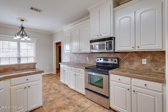 kitchen featuring crown molding, decorative light fixtures, appliances with stainless steel finishes, tile counters, and white cabinets