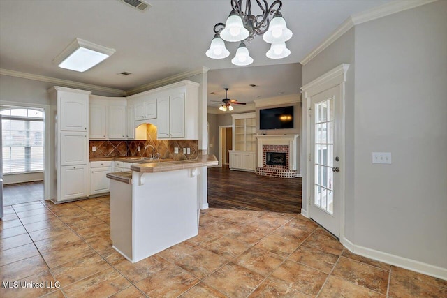 kitchen with sink, a breakfast bar area, white cabinets, a brick fireplace, and kitchen peninsula