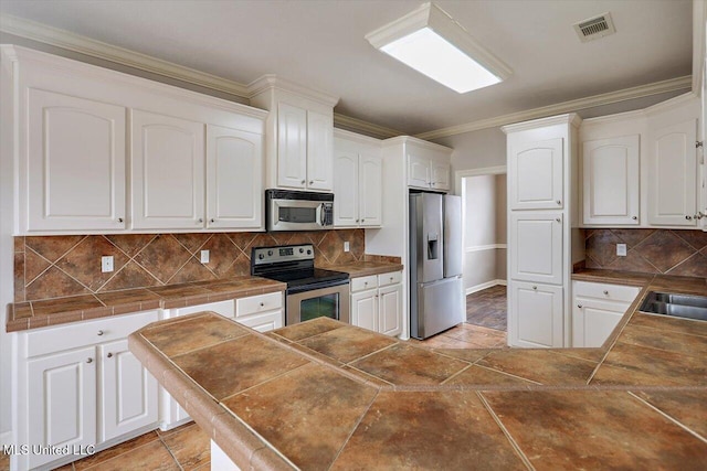 kitchen featuring white cabinetry, tile countertops, ornamental molding, and appliances with stainless steel finishes