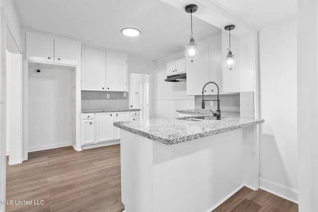 kitchen featuring hardwood / wood-style flooring, kitchen peninsula, sink, decorative light fixtures, and white cabinets